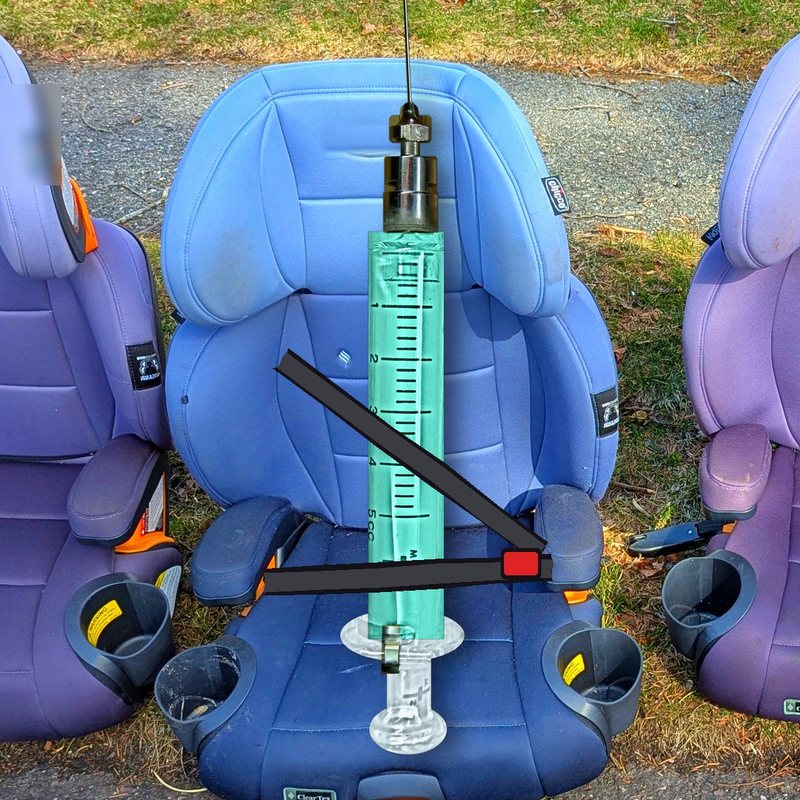 A syringe buckled into a real blue kid's booster seat on the grass.